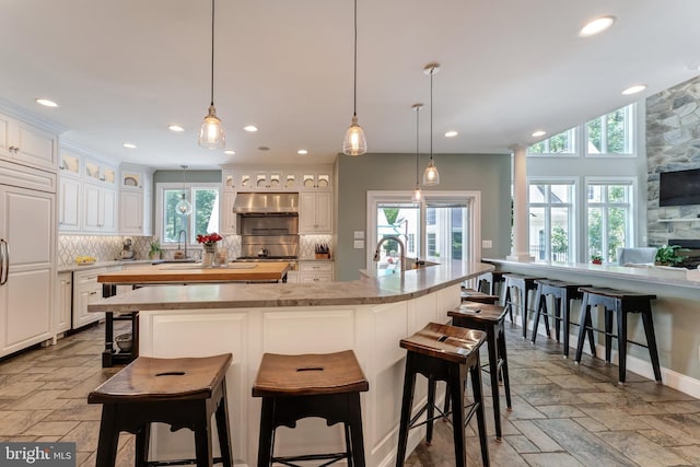 5026 Huntwood Manor Dr, Fairfax, VA 22030 - kitchen with under cabinet range hood, backsplash, a spacious island, stone tile floors, and a sink