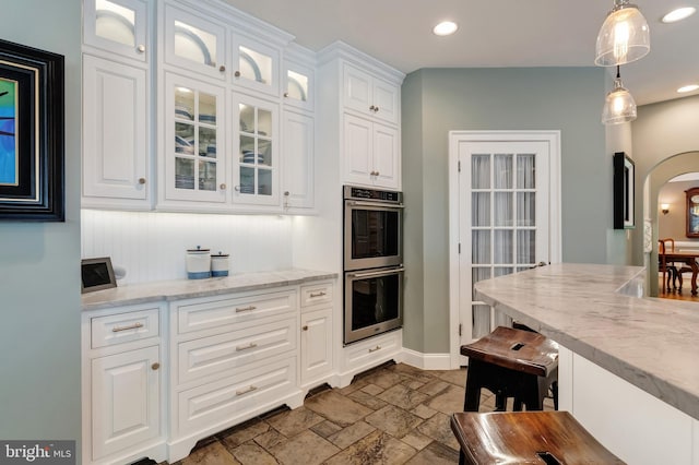 5026 Huntwood Manor Dr, Fairfax, VA 22030 - kitchen with stainless steel double oven, arched walkways, stone tile floors, white cabinetry, and glass insert cabinets