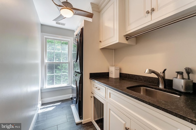 5026 Huntwood Manor Dr, Fairfax, VA 22030 - kitchen with stacked washer / dryer, a sink, baseboards, dark stone countertops, and white cabinetry