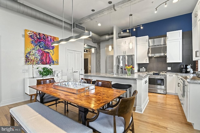 41 W Lemon St Unit 505, Lancaster, PA 17603 - kitchen featuring stainless steel appliances, wall chimney range hood, light wood-style floors, an island with sink, and white cabinets