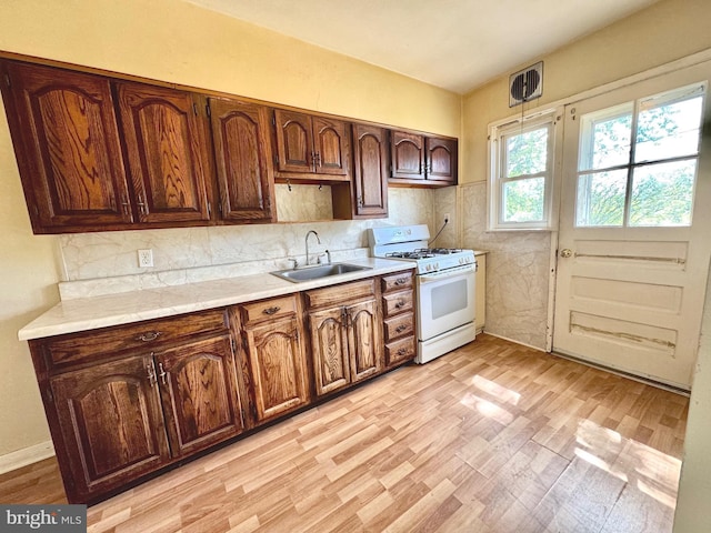 8024 Kimberly Rd, Dundalk, MD 21222 - kitchen featuring white gas stove, a sink, light countertops, light wood finished floors, and decorative backsplash