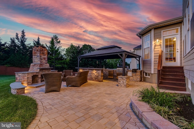 42720 Mount Auburn Pl, Broadlands, VA 20148 - patio terrace at dusk featuring an outdoor stone fireplace, exterior kitchen, a gazebo, a patio area, and entry steps