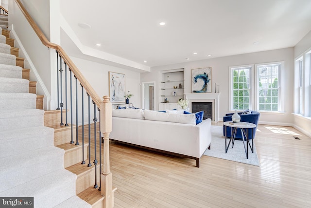 42720 Mount Auburn Pl, Broadlands, VA 20148 - living area featuring stairs, built in shelves, a glass covered fireplace, light wood-type flooring, and baseboards
