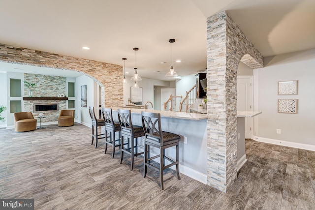 42720 Mount Auburn Pl, Broadlands, VA 20148 - kitchen with a kitchen breakfast bar, wood finished floors, arched walkways, a fireplace, and recessed lighting