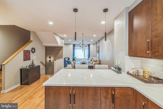 211 Brown St Unit 15, Philadelphia, PA 19123 - kitchen with a peninsula, brown cabinetry, light wood finished floors, light stone countertops, and a chandelier