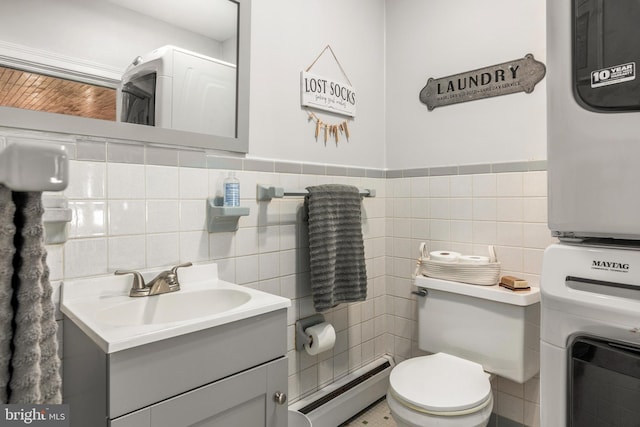 1110 Holland Ave, Cambridge, MD 21613 - half bath featuring a baseboard heating unit, stacked washer / dryer, tile walls, toilet, and vanity