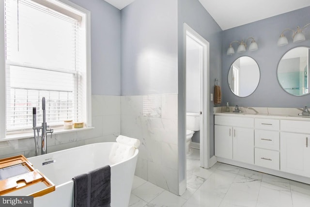 5E 27th St, Baltimore, MD 21218 - full bathroom with marble look tiles, double vanity, toilet, a soaking tub, and a wainscoted wall