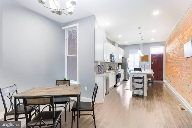 5E 27th St, Baltimore, MD 21218 - dining space featuring baseboards, brick wall, a chandelier, light wood-style floors, and recessed lighting
