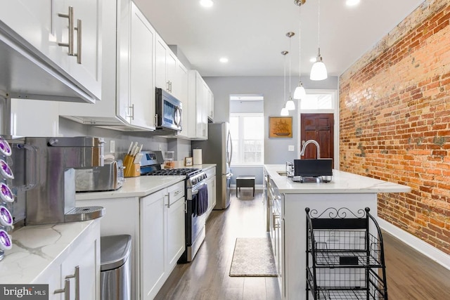 5E 27th St, Baltimore, MD 21218 - kitchen featuring stainless steel appliances, brick wall, wood finished floors, baseboards, and a center island with sink