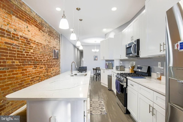 5E 27th St, Baltimore, MD 21218 - kitchen featuring appliances with stainless steel finishes, a sink, brick wall, wood finished floors, and a kitchen island with sink