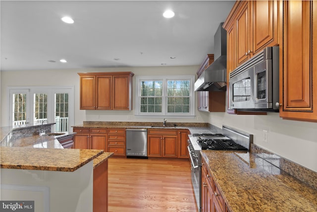 14603 Turner Wootton Pkwy, Upper Marlboro, MD 20774 - kitchen featuring stainless steel appliances, wall chimney exhaust hood, a sink, brown cabinetry, and light wood-style flooring