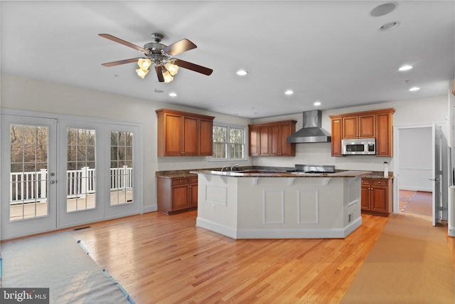 14603 Turner Wootton Pkwy, Upper Marlboro, MD 20774 - kitchen featuring wall chimney range hood, stainless steel microwave, light wood-style floors, ceiling fan, and a breakfast bar