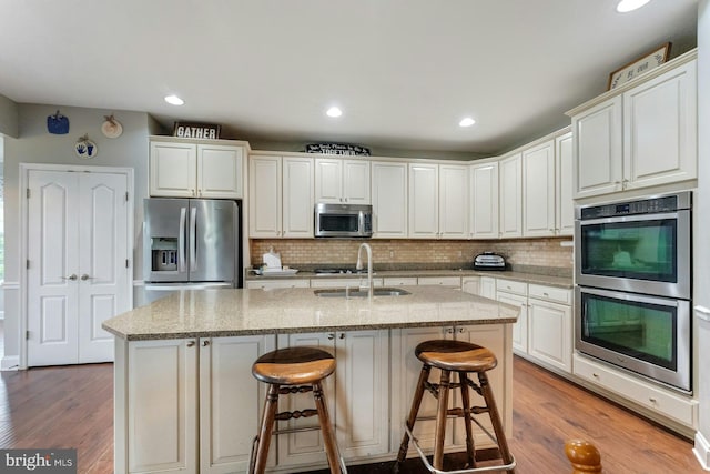 43268 Heavenly Cir, Leesburg, VA 20176 - kitchen featuring stainless steel appliances, a sink, backsplash, a kitchen island with sink, and wood finished floors