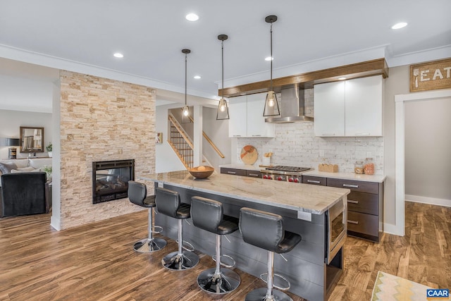 729 Highgate Row, Crozet, VA 22932 - kitchen featuring wall chimney range hood, ornamental molding, white cabinetry, a breakfast bar area, and decorative backsplash