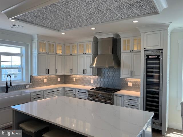 11 Selma Dr, Manahawkin, NJ 08050 - kitchen with high end stove, beverage cooler, wall chimney exhaust hood, a kitchen island, and decorative backsplash