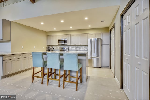 801 N Howard St Unit 305, Alexandria, VA 22304 - kitchen with appliances with stainless steel finishes, decorative backsplash, a breakfast bar area, a center island, and light tile patterned floors