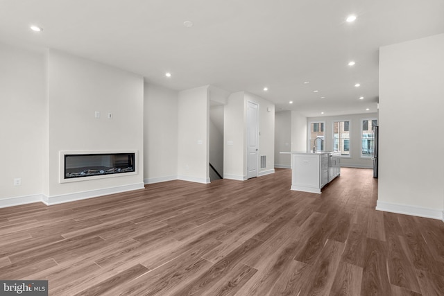 23062 Soaring Heights Ter, Ashburn, VA 20148 - unfurnished living room with recessed lighting, light wood-type flooring, a sink, baseboards, and a glass covered fireplace