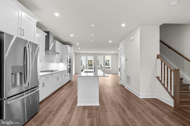23062 Soaring Heights Ter, Ashburn, VA 20148 - kitchen featuring appliances with stainless steel finishes, wall chimney range hood, a sink, a kitchen island with sink, and white cabinetry