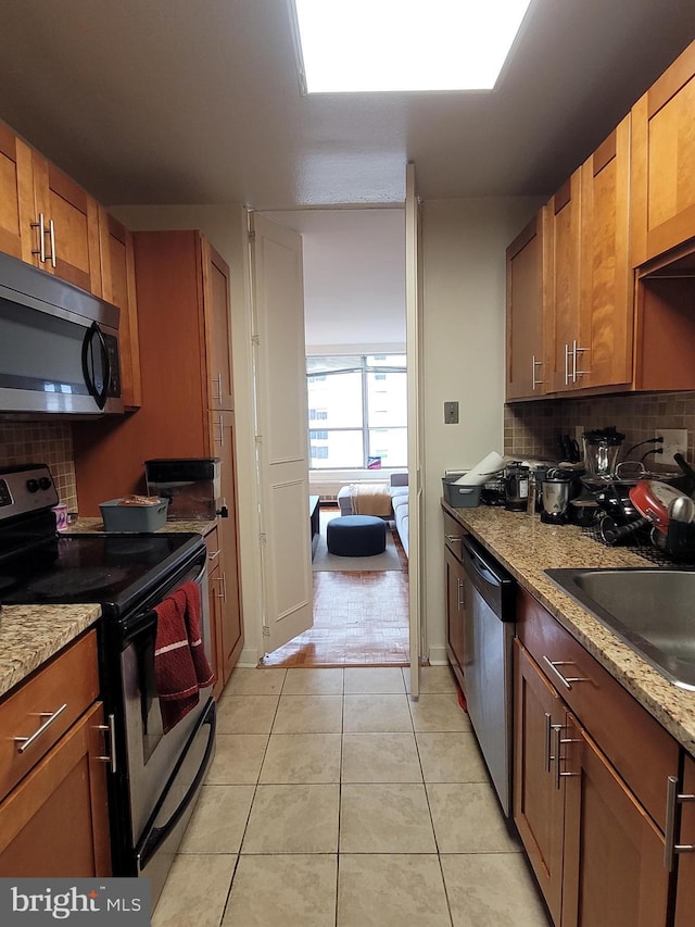224 W Rittenhouse Sq Unit 2701, Philadelphia, PA 19103 - kitchen with appliances with stainless steel finishes, decorative backsplash, light tile patterned flooring, light stone counters, and brown cabinets