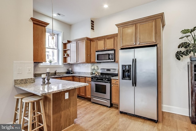 251 8th St NE, Washington, DC 20002 - kitchen featuring appliances with stainless steel finishes, a peninsula, brown cabinets, light stone countertops, and recessed lighting