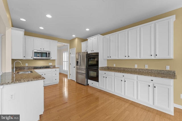 327 Astilbe Dr, Kennett Square, PA 19348 - kitchen featuring a sink, black appliances, light wood finished floors, white cabinets, and stone countertops