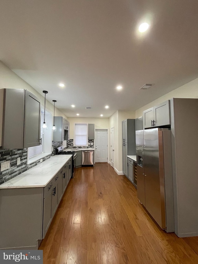 5724 Pine St, Philadelphia, PA 19143 - kitchen featuring gray cabinetry, appliances with stainless steel finishes, dark wood finished floors, decorative backsplash, and hanging light fixtures
