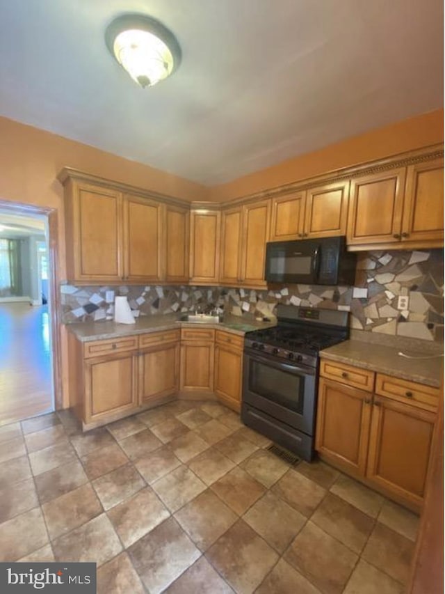 4216 Wyalusing Ave, Philadelphia, PA 19104 - kitchen featuring stainless steel range with gas cooktop, black microwave, backsplash, and brown cabinetry