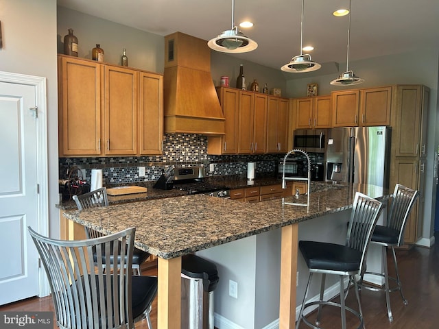 23294 Evening Primrose Sq, Brambleton, VA 20148 - kitchen featuring custom range hood, appliances with stainless steel finishes, tasteful backsplash, brown cabinets, and a breakfast bar