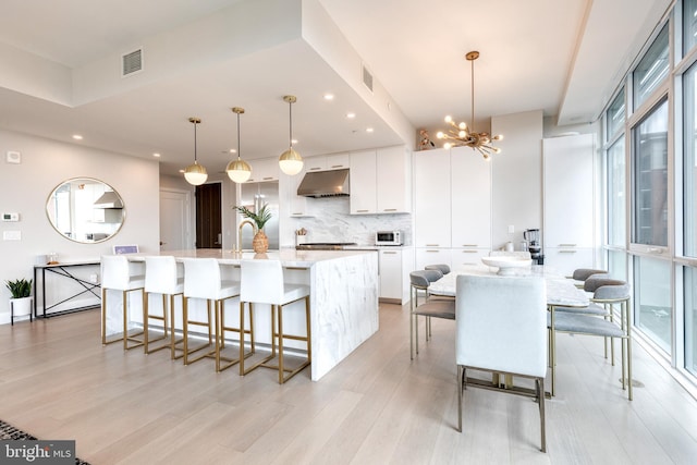 1330 Lancaster St Unit C701, Baltimore, MD 21231 - kitchen featuring under cabinet range hood, light wood-type flooring, white cabinets, tasteful backsplash, and a large island