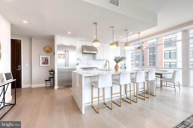 1330 Lancaster St Unit C701, Baltimore, MD 21231 - kitchen featuring under cabinet range hood, built in fridge, light wood-type flooring, white cabinets, and a breakfast bar