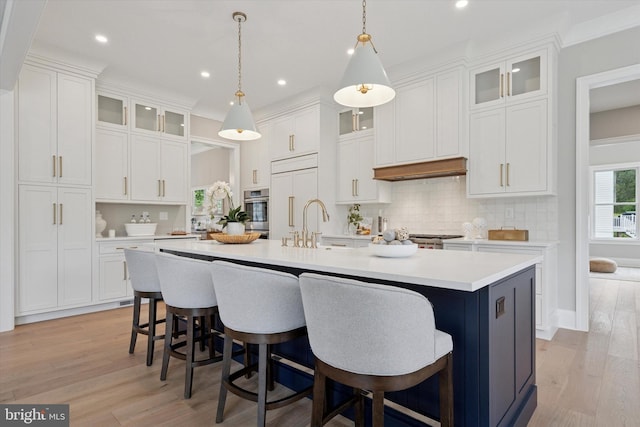 215 S Spring Mill Rd, Villanova, PA 19085 - kitchen with oven, an island with sink, light countertops, light wood-style floors, and white cabinets