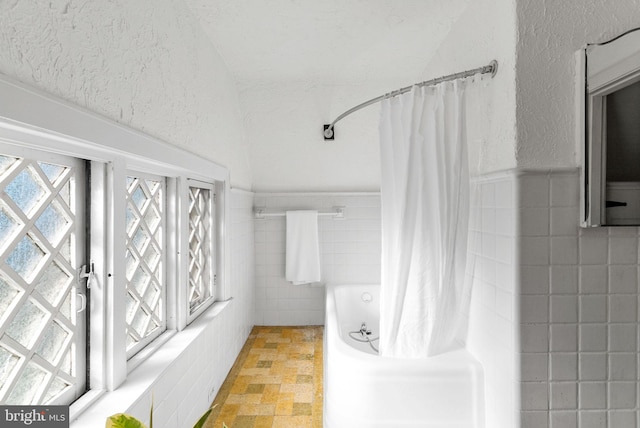 8515 Seminole St, Philadelphia, PA 19118 - full bathroom featuring tile walls, shower / bathtub combination with curtain, stone finish floors, and a wainscoted wall