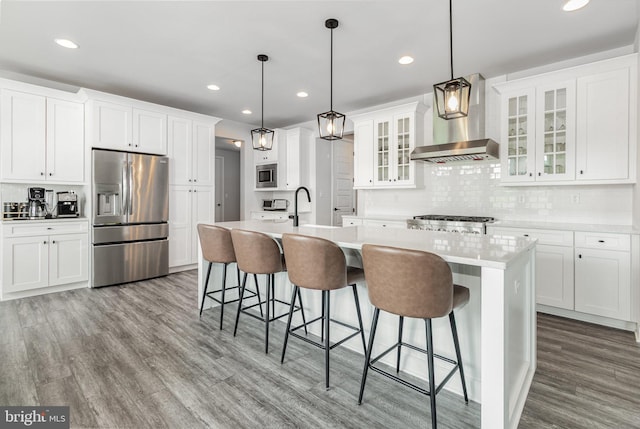 220 Moorefield St, Mechanicsburg, PA 17055 - kitchen featuring appliances with stainless steel finishes, wall chimney exhaust hood, wood finished floors, a kitchen island with sink, and backsplash