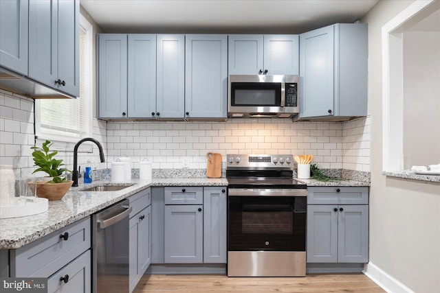 1202 Dukeland St, Baltimore, MD 21216 - kitchen with appliances with stainless steel finishes, a sink, light wood-style flooring, backsplash, and light stone countertops