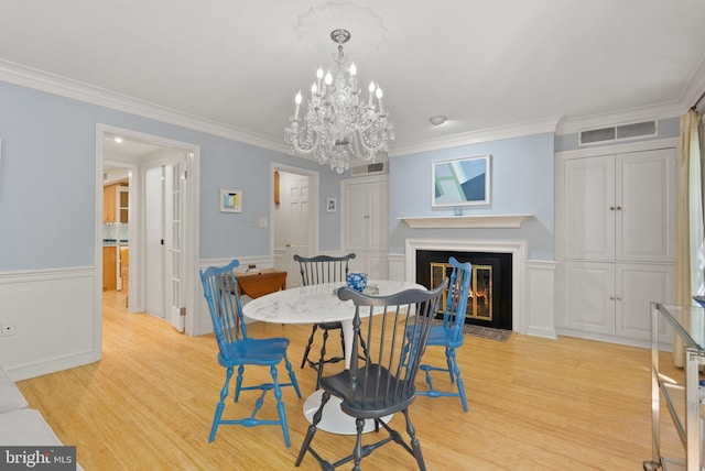 116 Cameron Mews, Alexandria, VA 22314 - dining space featuring light wood-style flooring, crown molding, a wainscoted wall, a fireplace with flush hearth, and a chandelier