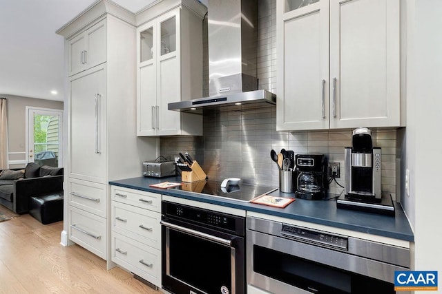 15 Trillium Close, Wintergreen Resort, VA 22967 - kitchen featuring wall chimney range hood, black appliances, dark countertops, decorative backsplash, and light wood-style flooring