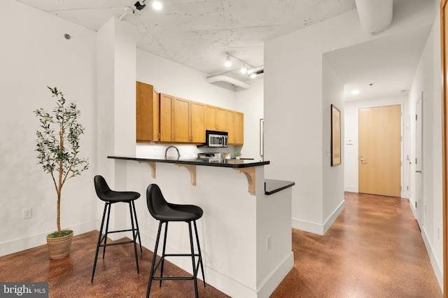 1700 Kalorama Rd NW Unit 206, Washington, DC 20009 - kitchen with stainless steel microwave, a breakfast bar, dark countertops, baseboards, and a peninsula