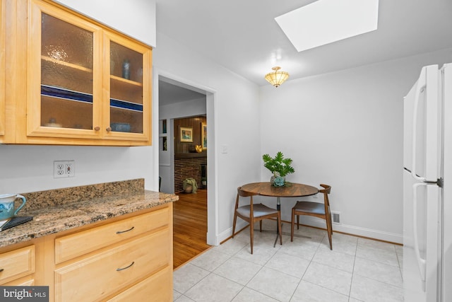 8008 Park Crest Dr, Silver Spring, MD 20910 - kitchen featuring freestanding refrigerator, a skylight, glass insert cabinets, light stone countertops, and light tile patterned floors