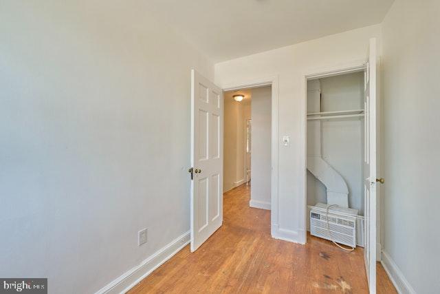 66 Allison St NE, Washington, DC 20011 - unfurnished bedroom featuring a closet, light wood-type flooring, baseboards, and a wall mounted air conditioner
