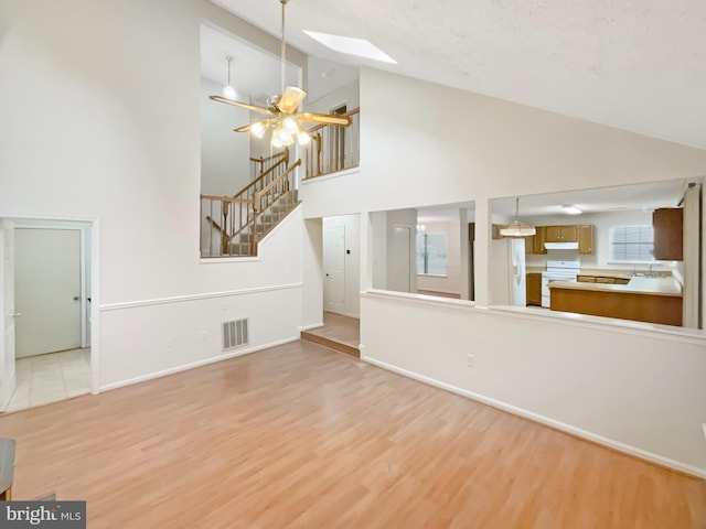 6502 Elk Ct, Waldorf, MD 20603 - unfurnished living room featuring high vaulted ceiling, a skylight, stairs, light wood-style floors, and baseboards