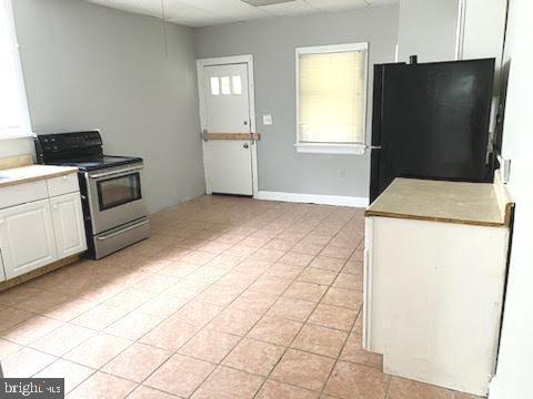 1364 Park Blvd, Camden, NJ 08103 - kitchen with stainless steel electric stove, freestanding refrigerator, white cabinets, light tile patterned flooring, and light countertops