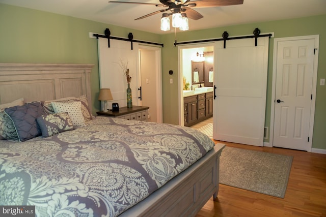 457 Langley Rd, Pittsgrove, NJ 08318 - bedroom with a barn door, wood finished floors, ensuite bath, ceiling fan, and a sink