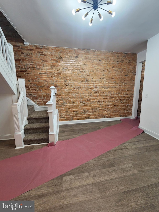 2218 Ruskin Ave, Baltimore, MD 21217 - unfurnished living room featuring wood finished floors, baseboards, a chandelier, stairs, and brick wall