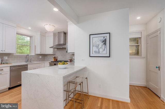 3709 Jocelyn St NW, Washington, DC 20015 - kitchen with appliances with stainless steel finishes, wall chimney exhaust hood, a sink, white cabinetry, and a kitchen bar
