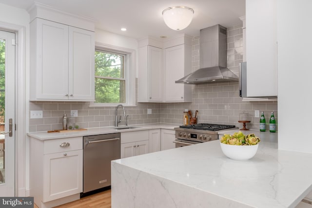3709 Jocelyn St NW, Washington, DC 20015 - kitchen with wall chimney exhaust hood, stainless steel appliances, a sink, a peninsula, and white cabinets