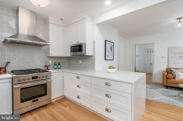 3709 Jocelyn St NW, Washington, DC 20015 - kitchen with stainless steel appliances, wall chimney range hood, light wood-style floors, a peninsula, and white cabinetry