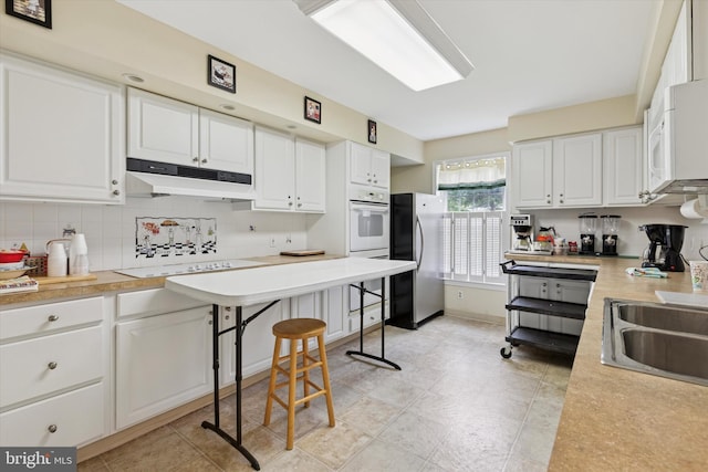 649 Brandon Rd, Eagleville, PA 19403 - kitchen with under cabinet range hood, white appliances, white cabinets, light countertops, and backsplash