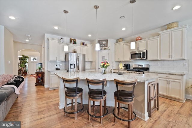 5544 Old Colony Ct, White Plains, MD 20695 - kitchen featuring stainless steel appliances, arched walkways, backsplash, a center island with sink, and light wood-type flooring