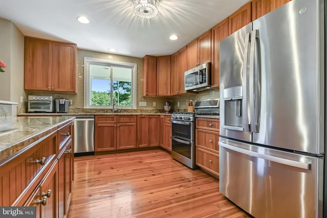 205 Mallard Dr, Stevensville, MD 21666 - kitchen featuring appliances with stainless steel finishes, brown cabinets, light stone counters, tasteful backsplash, and light wood-style flooring