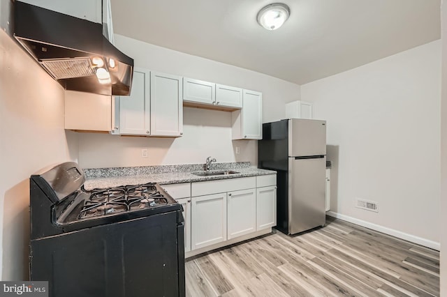 118 N Hilton St, Baltimore, MD 21229 - kitchen with black range with gas cooktop, freestanding refrigerator, exhaust hood, a sink, and light wood-style flooring